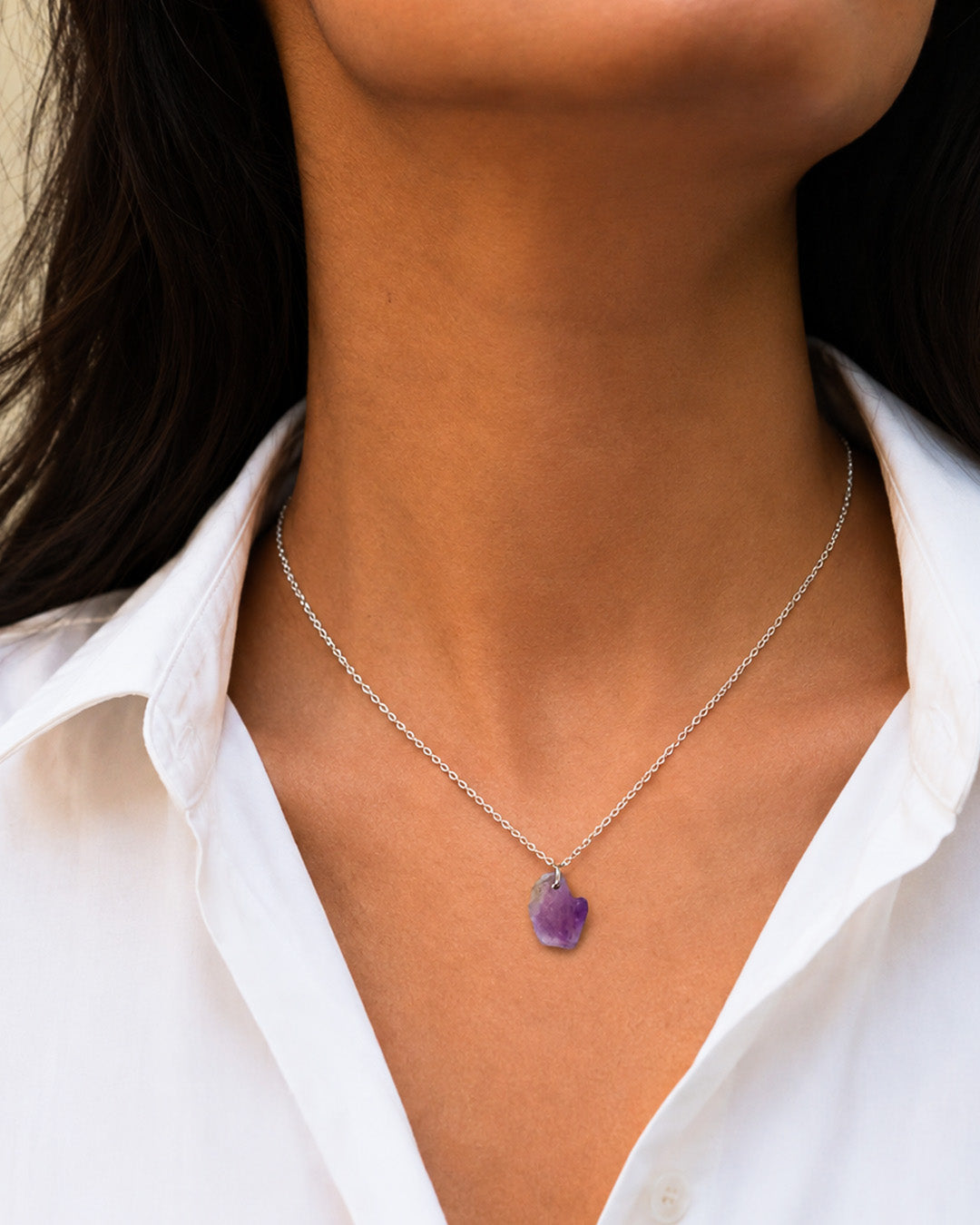 Necklace with a purple pendant worn by a person in a white shirt