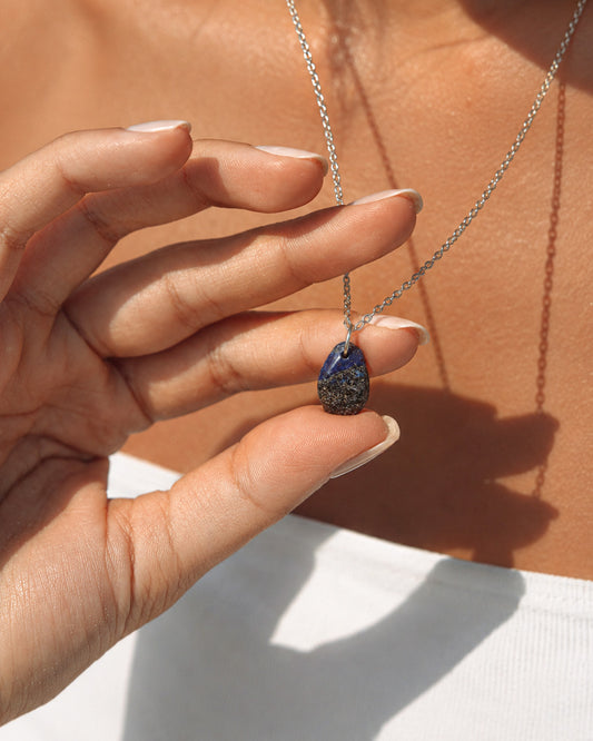Lapis Lazuli Hand holding a necklace with a blue pendant against a neutral background