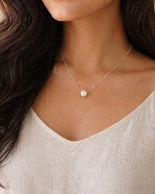 Woman wearing a necklace with a pearl pendant against a neutral background