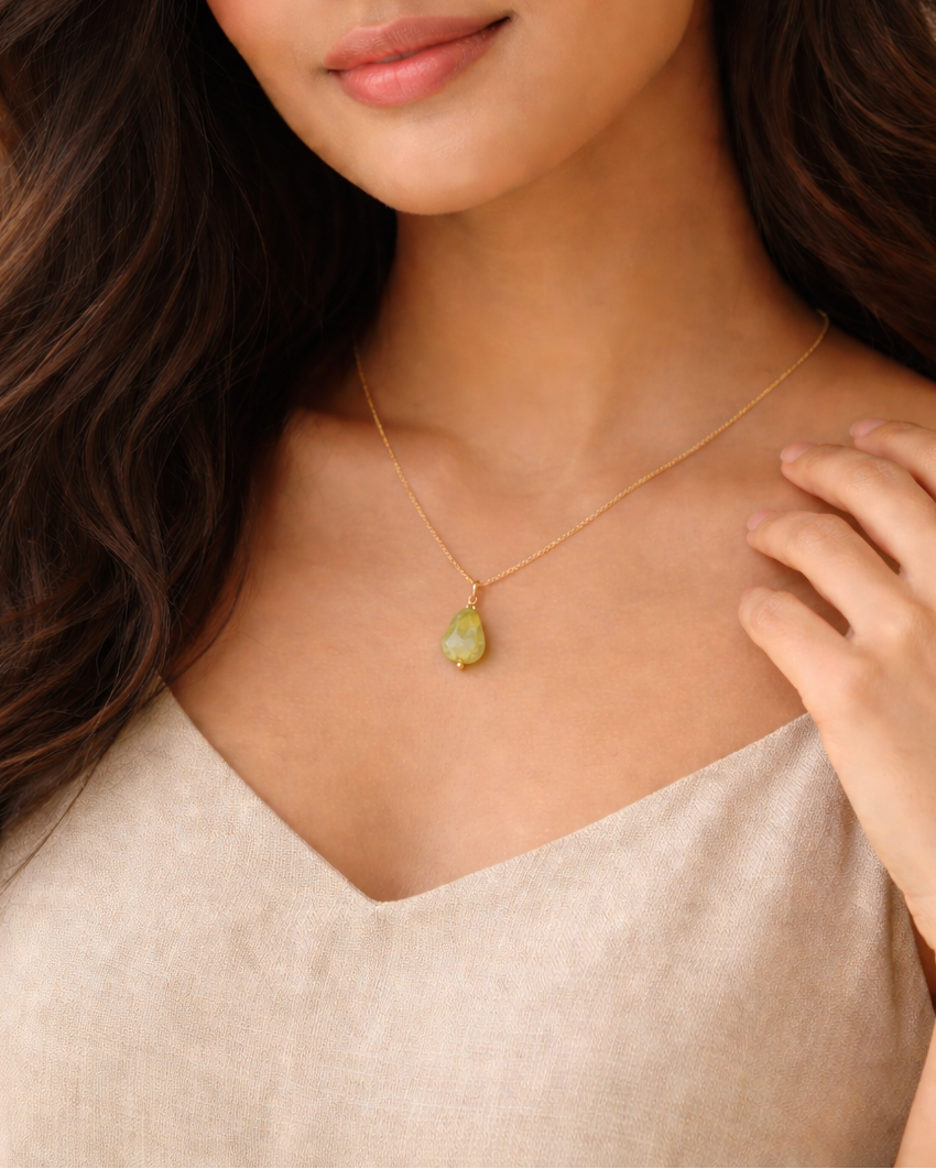 Woman wearing a necklace with a green pendant against a neutral background