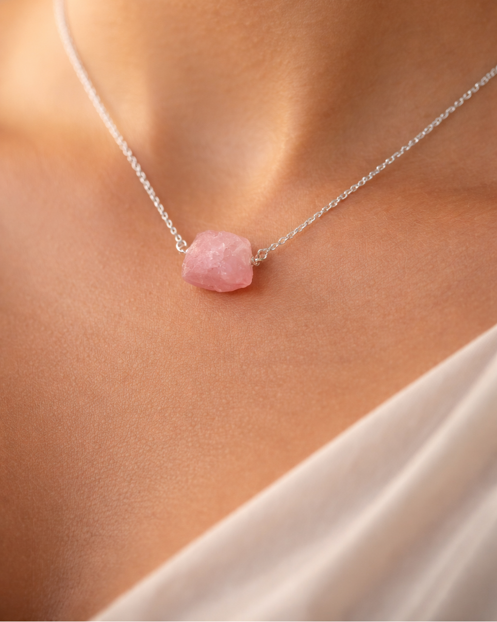 Necklace with a pink stone pendant on a person wearing a white top.