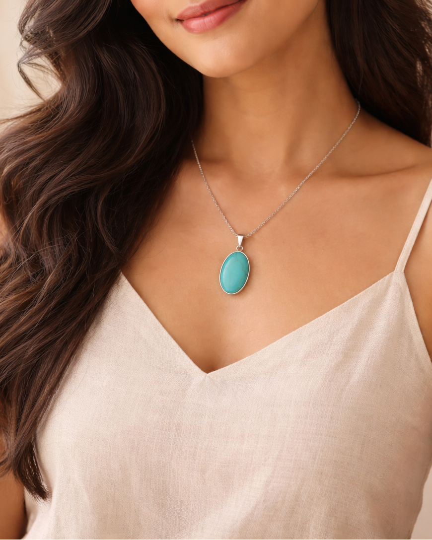 Woman wearing a necklace with a turquoise pendant against a neutral background