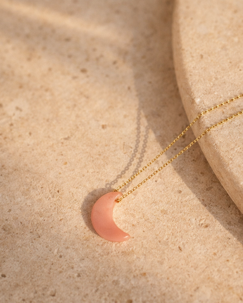 pink opal luna moon pendant necklace on gold chain placed on beige surface showing soft blush pink stone