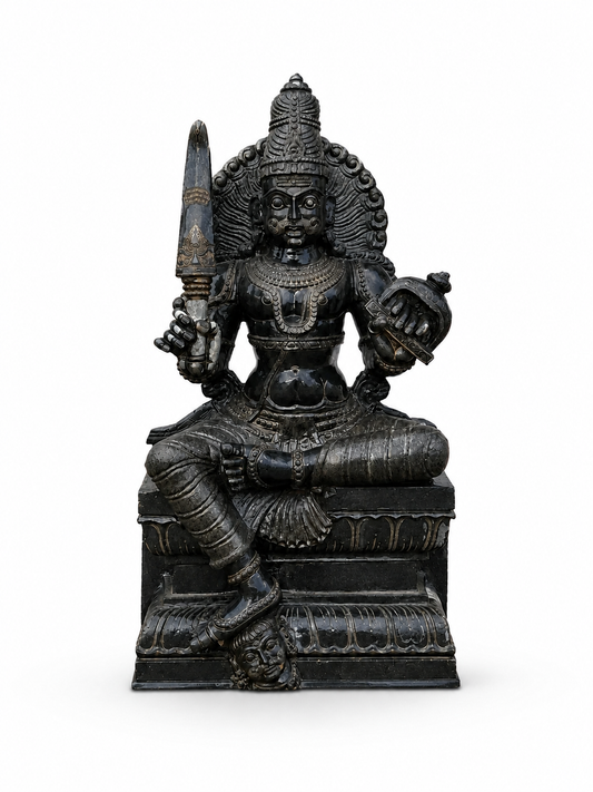 A dark metallic Hindu deity statue seated on a pedestal, holding a sword and an axe, photographed against a plain white background.