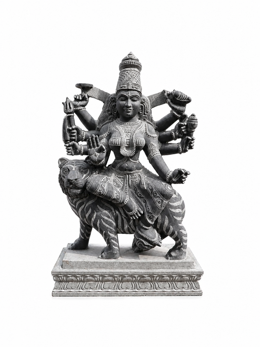 A dark gray stone statue of a multi-armed Hindu goddess riding a tiger, set against a plain white background.