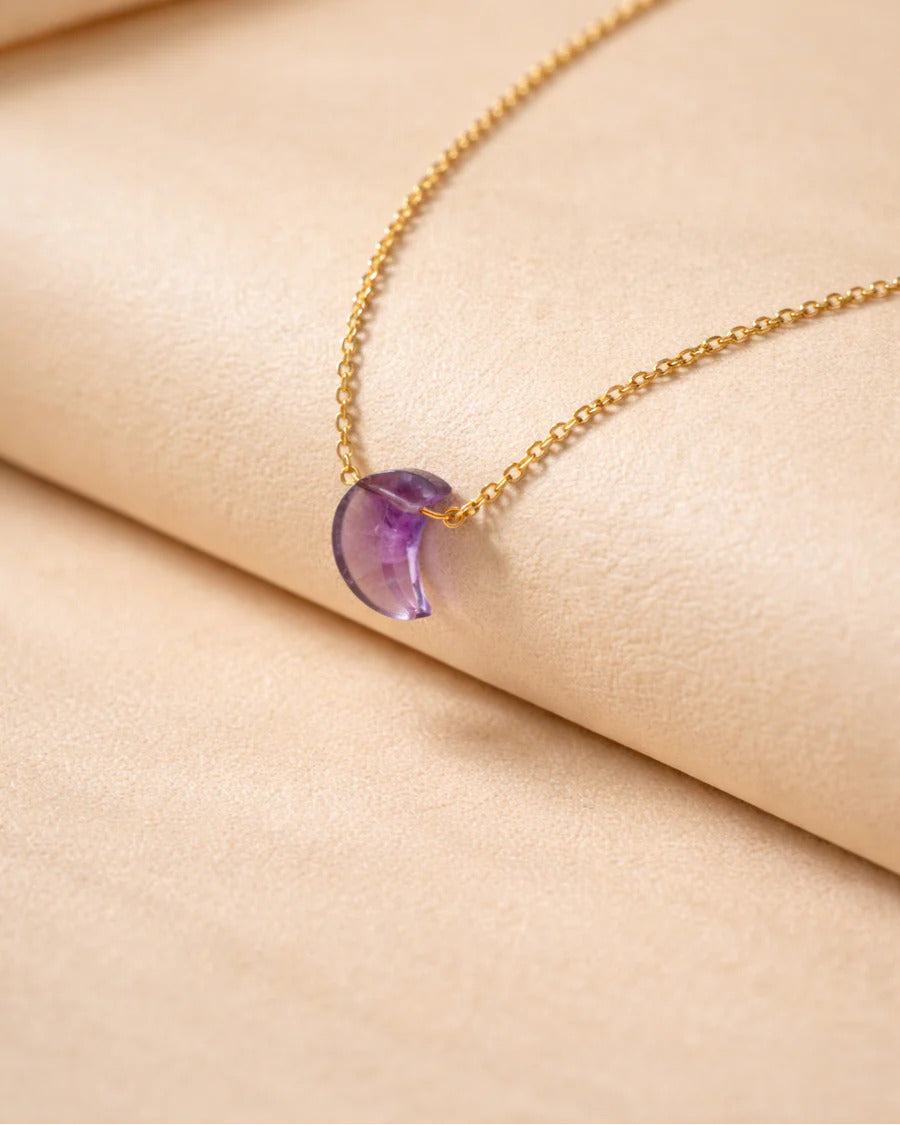 Gold necklace with a purple gemstone on a beige fabric background