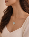 Woman wearing a gold necklace with a pendant against a neutral background