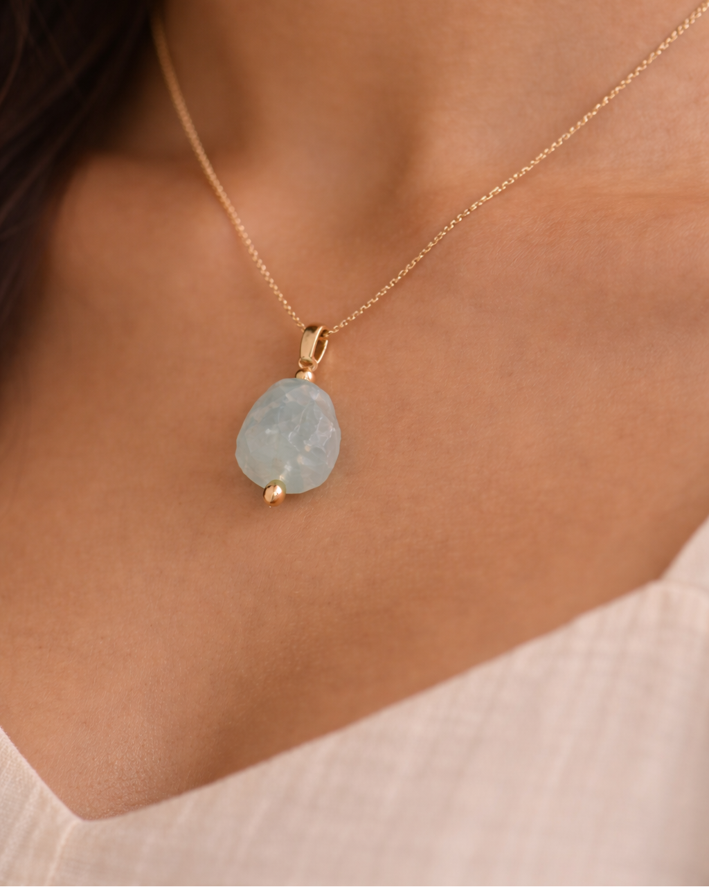 Necklace with a light blue pendant on a person wearing a white top.