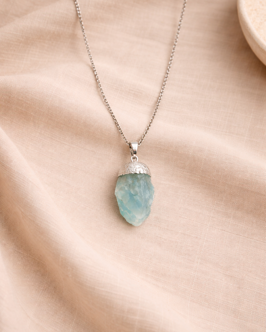 Aquamarine pendant with stainless steel chain on beige background