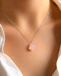 Raw Rose Quartz Necklace with a pink stone pendant on a person wearing a white top.