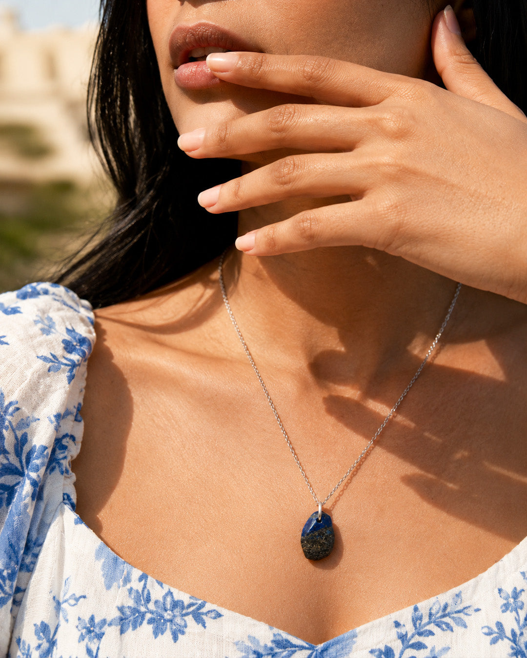 Lapis Lazuli Woman wearing a silver necklace with a dark pendant, outdoors.