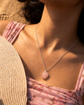 Close-up of a person wearing a pink pendant Raw Rose Quartz necklace with a blurred background