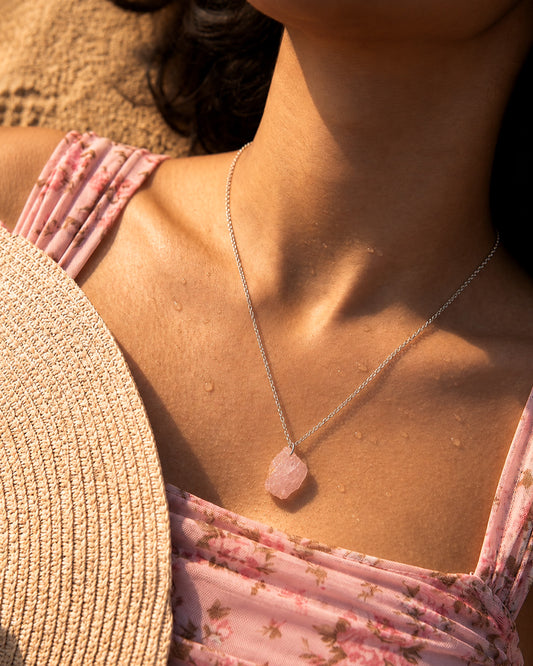 Close-up of a person wearing a pink pendant Raw Rose Quartz necklace with a blurred background