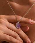 Necklace with a purple pendant held by a hand against a neutral background