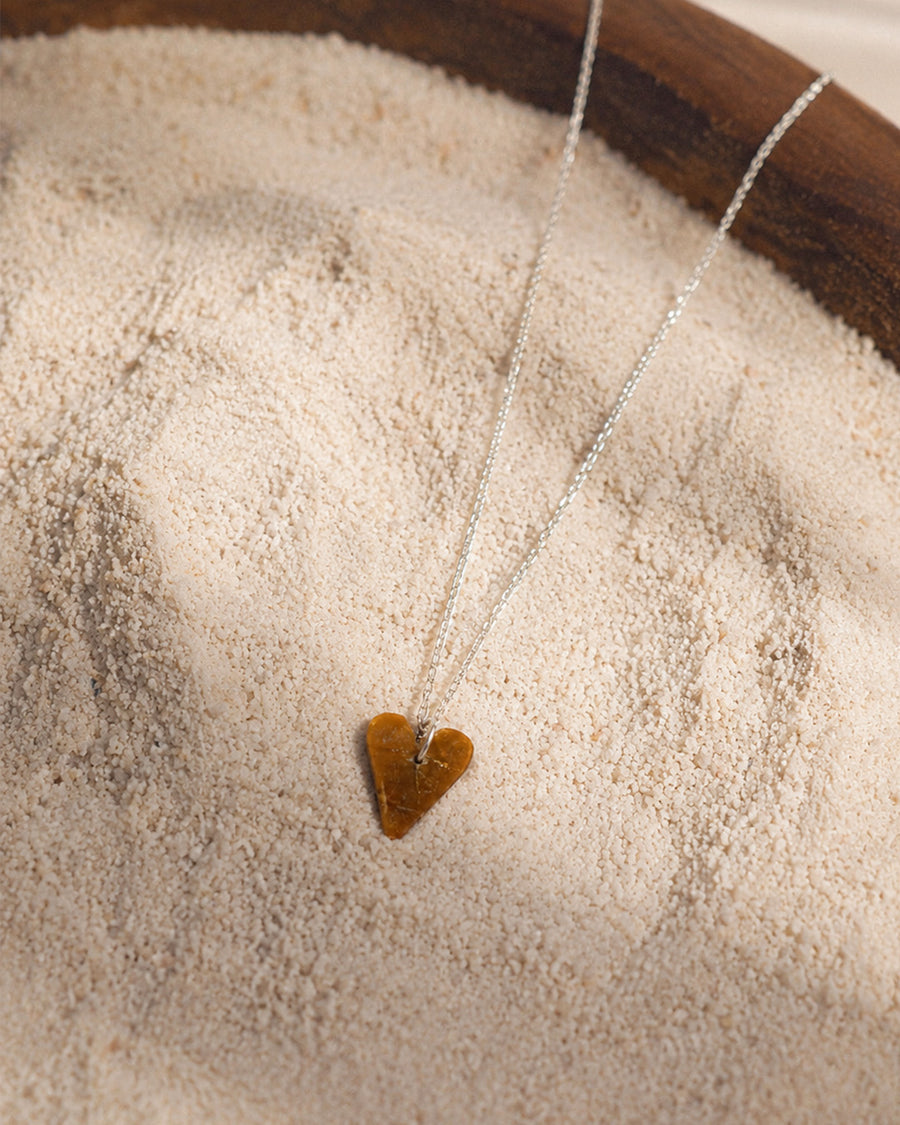 Tiger Eye Heart-shaped pendant necklace on a wooden surface with sand