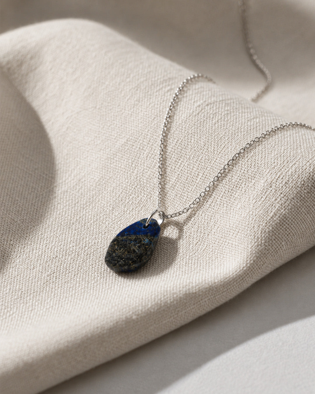 Lapis Lazuli Necklace with a teardrop-shaped pendant on a textured beige surface