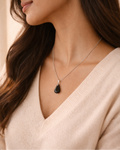 Woman wearing a necklace with a black pendant against a neutral background
