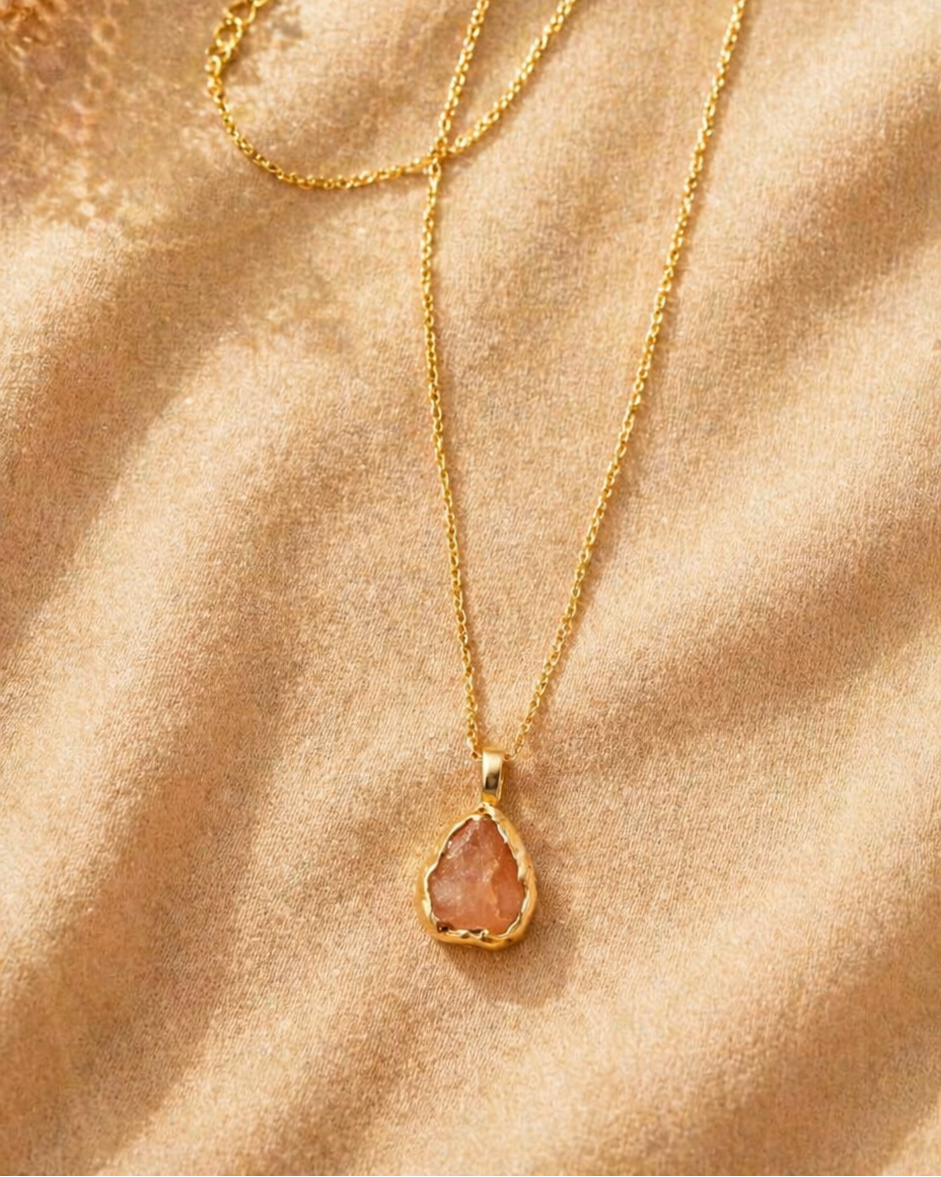 Gold necklace with a teardrop-shaped pendant on a beige fabric background