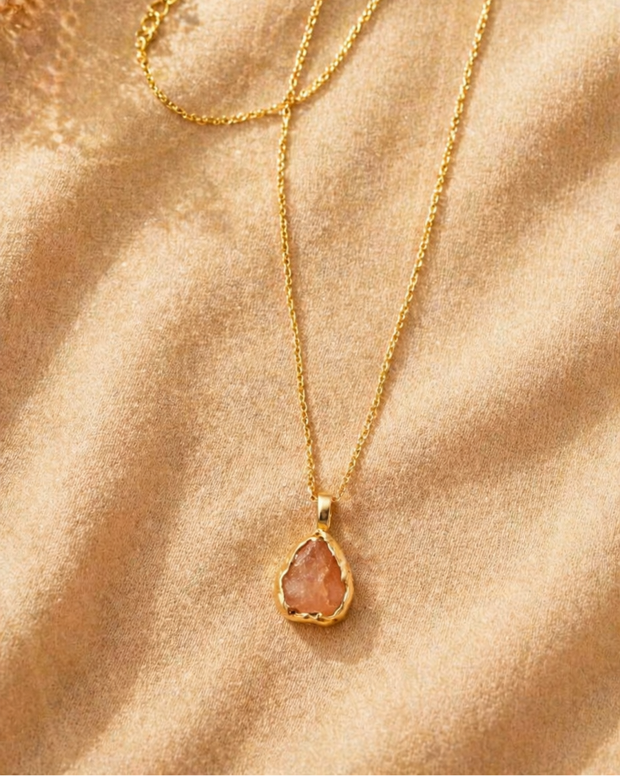 Gold necklace with a teardrop-shaped pendant on a beige fabric background