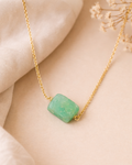 Gold necklace with a green stone pendant on a beige background