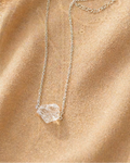 Silver necklace with a clear pendant on a beige fabric background