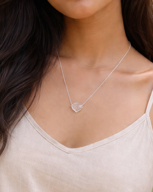 Woman wearing a beige tank top and a necklace with a heart pendant, standing outdoors.