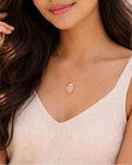 Woman wearing a necklace with a heart pendant against a neutral background