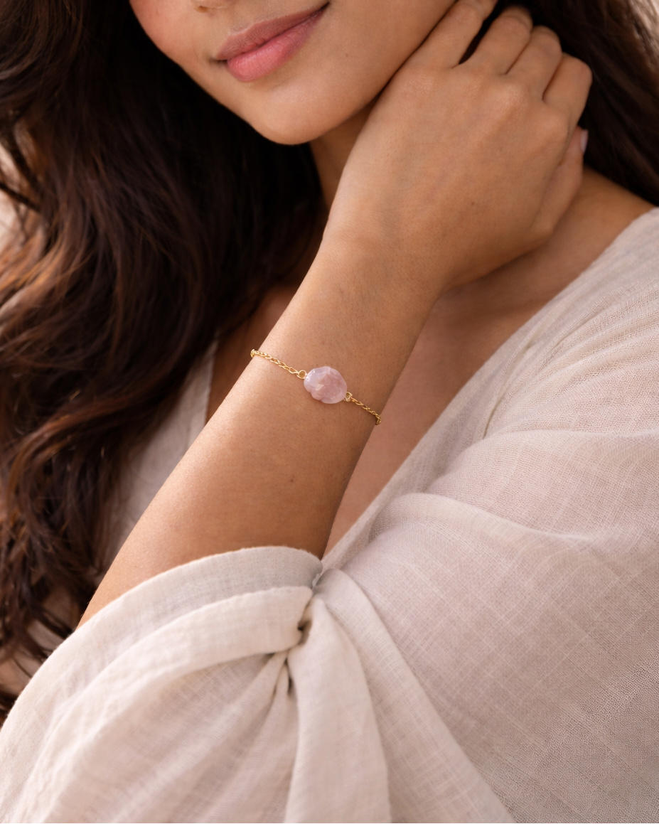 Woman wearing a gold bracelet with a pink stone on a neutral background
