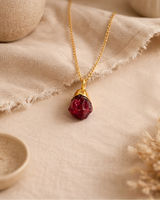 Raw garnet gold plated necklace on beige aesthetic background