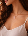 Woman wearing a delicate necklace with a pink pendant against a neutral background