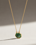 Gold necklace with a green pendant on a neutral background
