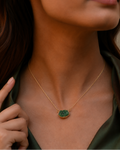 Close-up of a person wearing a gold necklace with a green pendant.