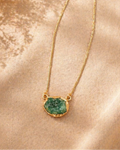 Gold necklace with a green pendant on a beige fabric background