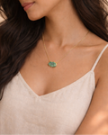 Woman wearing a gold necklace with a green pendant against a neutral background
