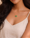 Woman wearing a necklace with a green pendant against a neutral background