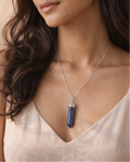Woman wearing a necklace with a blue pendant against a beige background