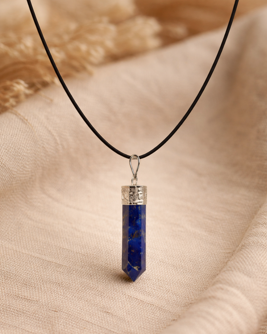 Blue crystal pendant on a black cord against a beige fabric background