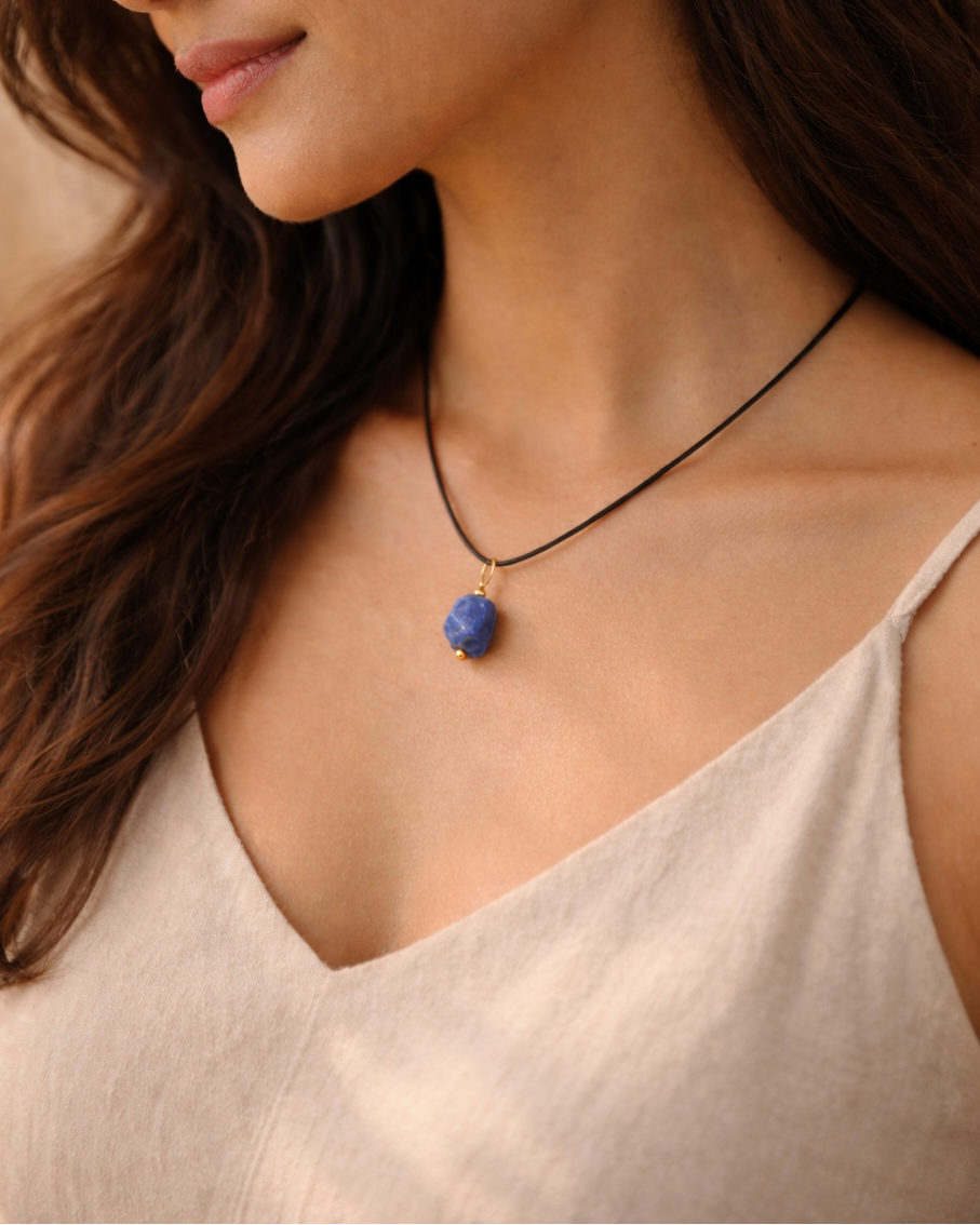 Woman wearing a necklace with a blue pendant against a neutral background