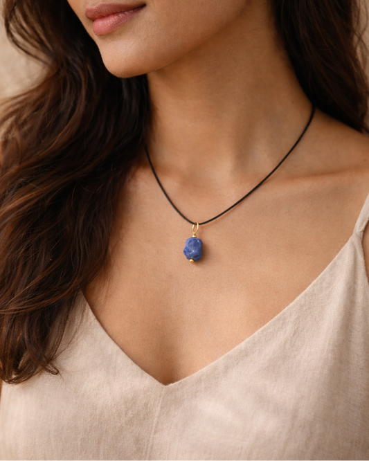 Woman wearing a necklace with a blue pendant against a neutral background