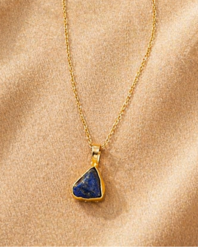 Gold necklace with a blue pendant on a beige fabric background