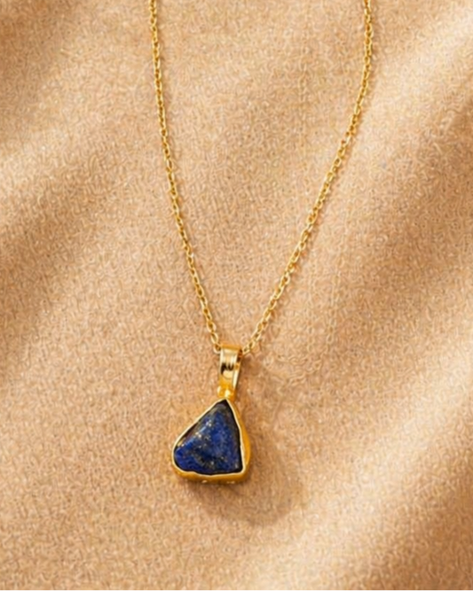 Gold necklace with a blue pendant on a beige fabric background