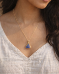 Woman wearing a gold necklace with a blue pendant against a neutral background