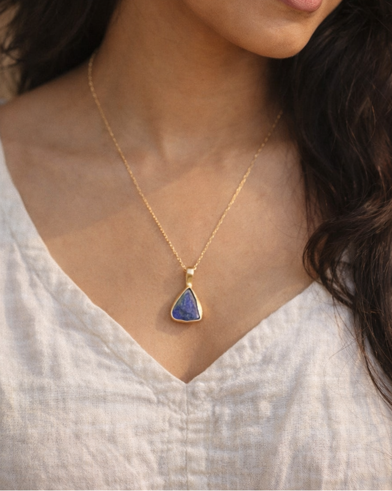 Woman wearing a gold necklace with a blue pendant against a neutral background