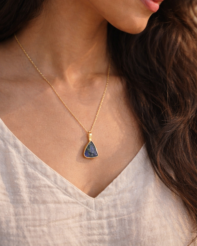Woman wearing a gold necklace with a blue pendant against a neutral background