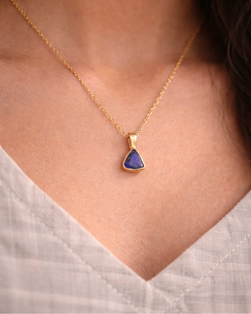 Gold necklace with a blue pendant worn by a person