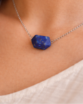 Necklace with a blue stone pendant on a person wearing a white top.