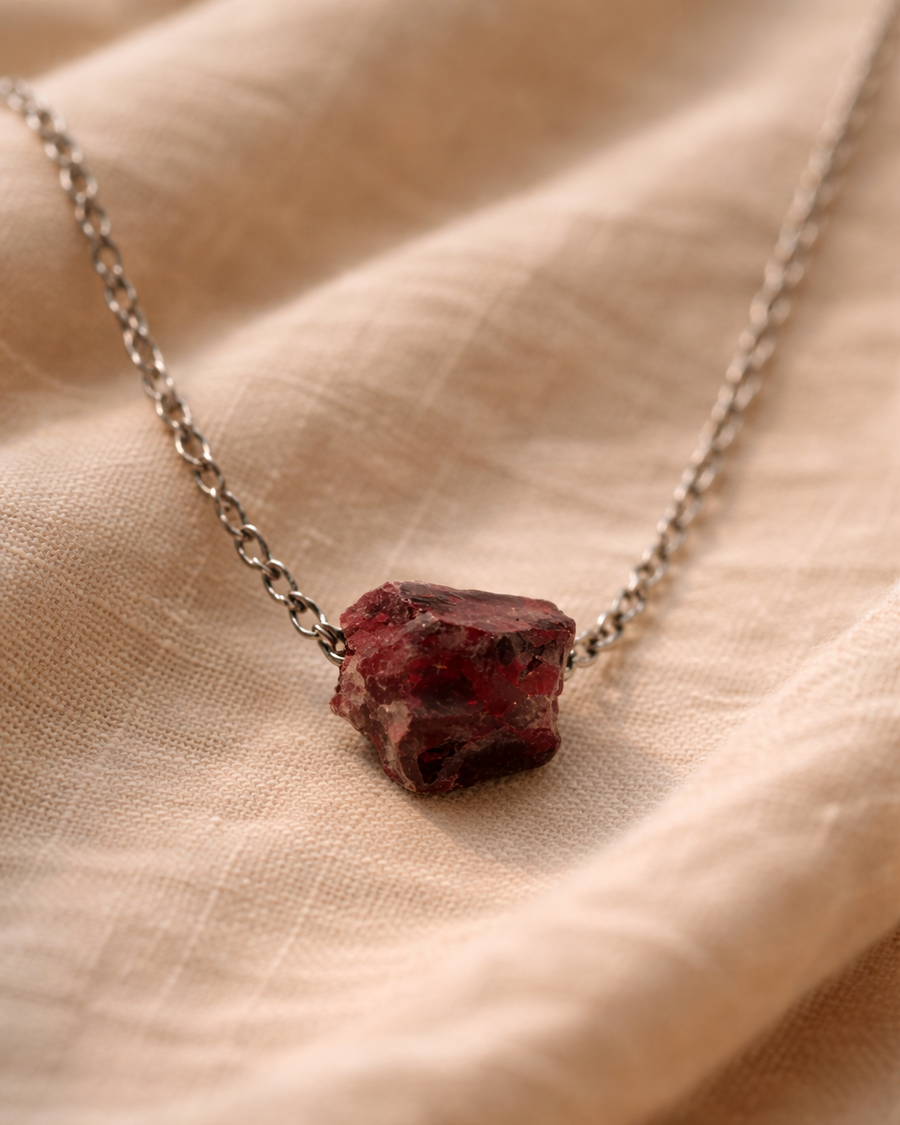 Natural garnet stone pendant with stainless steel chain on beige background