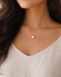 Woman wearing a necklace with a pearl pendant against a neutral background