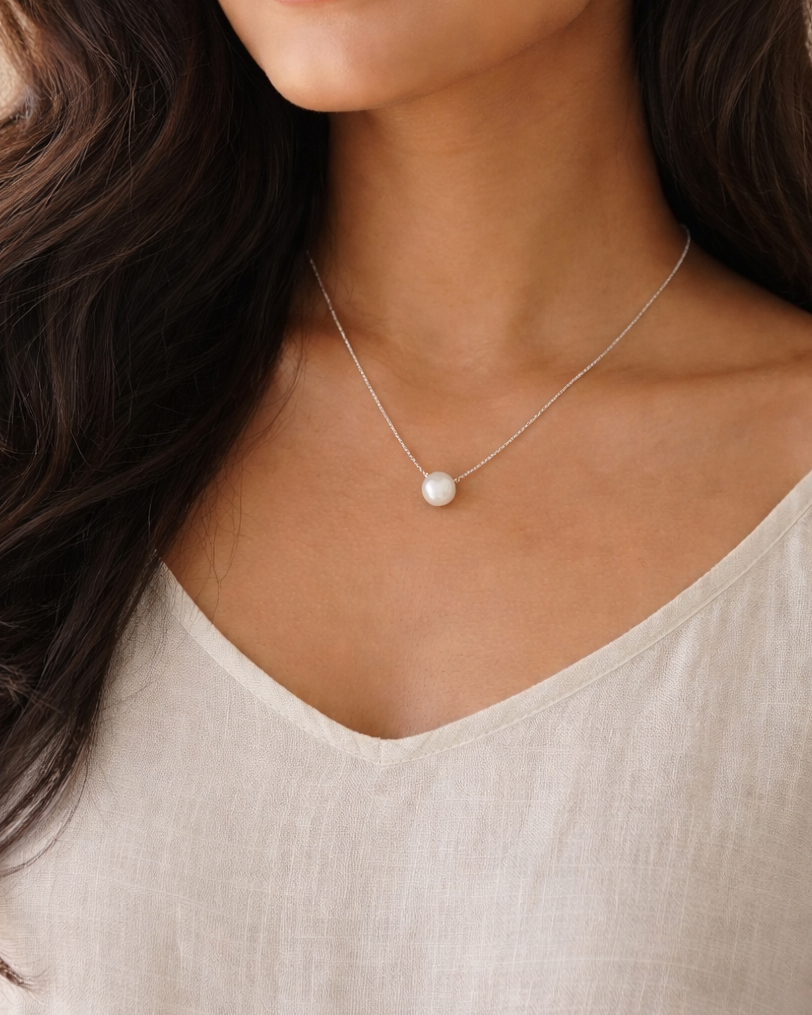 Woman wearing a necklace with a pearl pendant against a neutral background