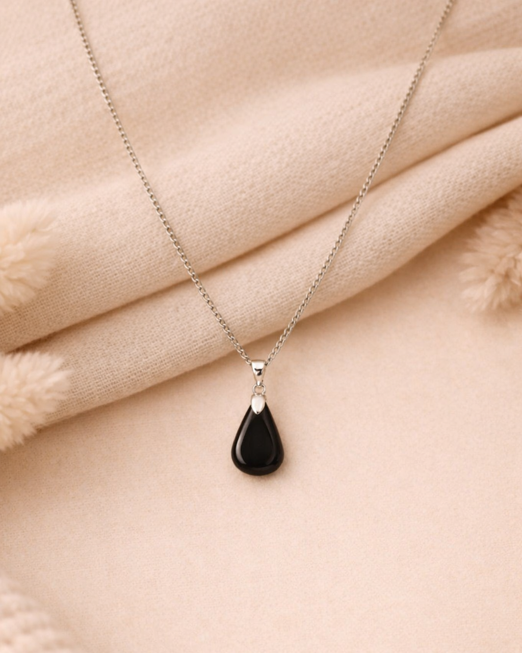 Necklace with a black teardrop pendant on a beige fabric background